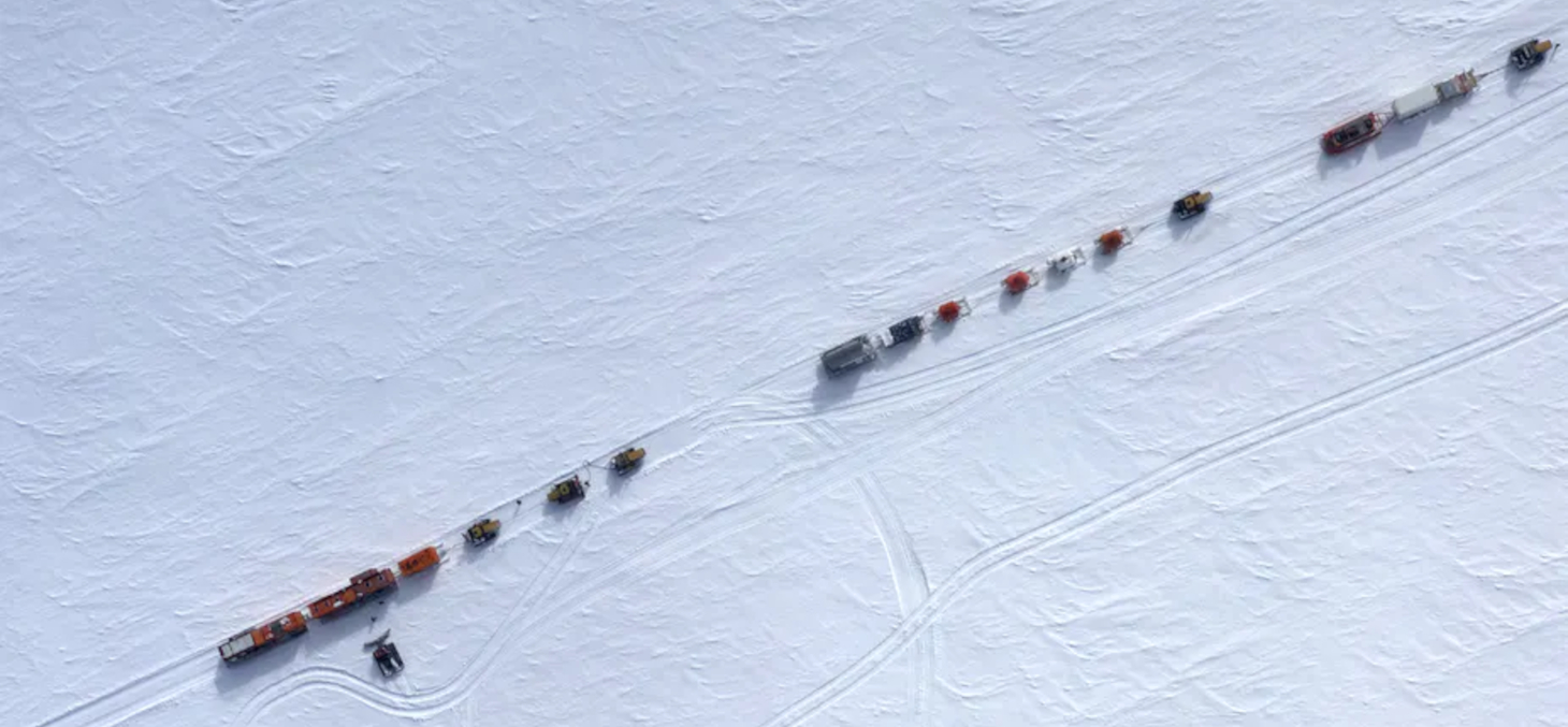 Vue aérienne du raid scientifique EAIIST prise par drone alors qu’il évolue sur le plateau Antarctique autour de 78 °S. Le raid est composé de trois convois comprenant les espaces de vie et l’énergie (en bas à gauche), les cuves de fioul (milieu) et l’équ